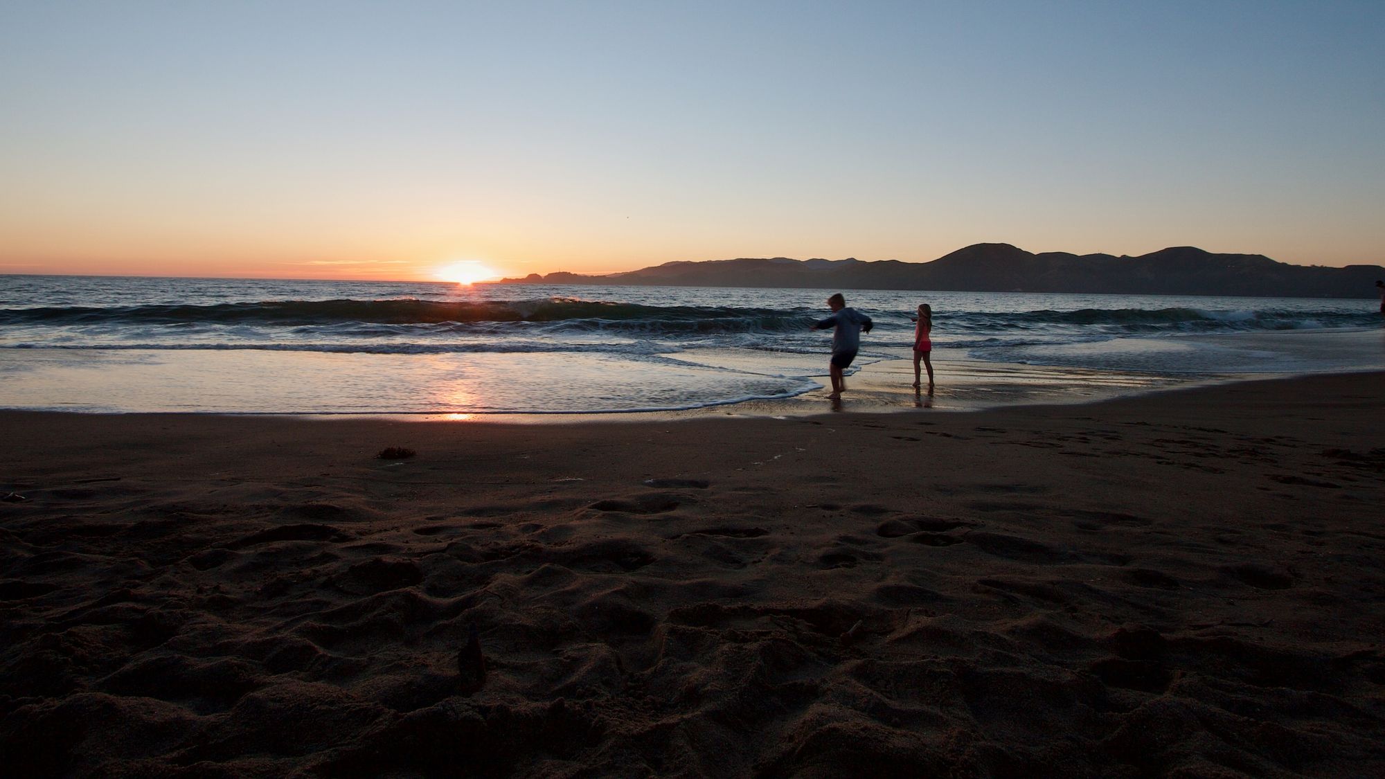 Two children dancing wit the waves at sunset on Pacific Beach in San Francisco, California